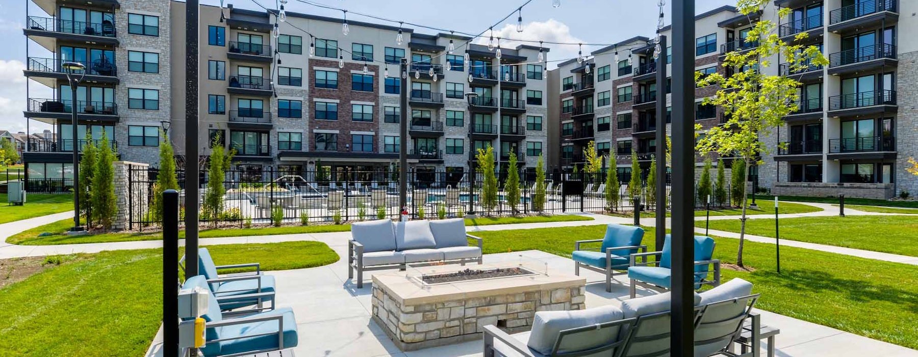An outdoor lounge with a fire pit, couches and chairs at Reflections luxury apartments in Kansas.